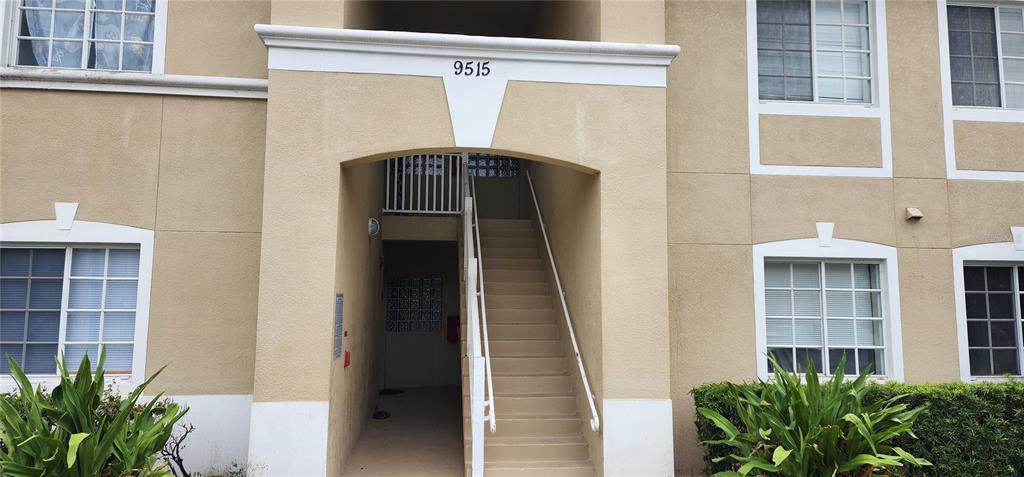 A beige apartment building exterior features a central staircase leading to an entrance with number 9515 — 9515 GROVEDALE CIRCLE UNIT 101, RIVERVIEW, FL