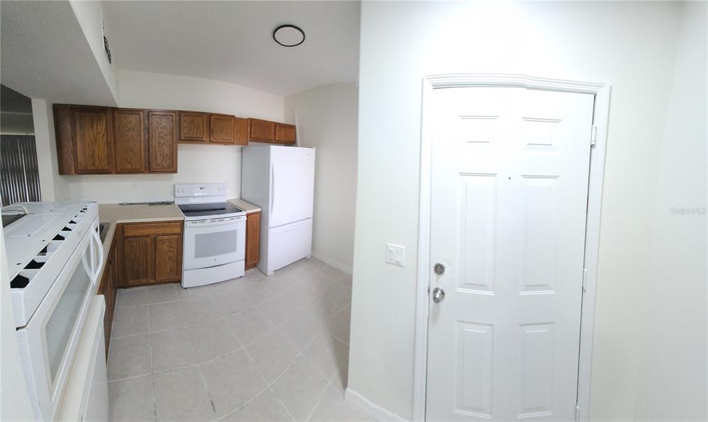 A kitchen with wood cabinets, white appliances, and light tile flooring near an entry door — 9515 GROVEDALE CIRCLE UNIT 101, RIVERVIEW, FL