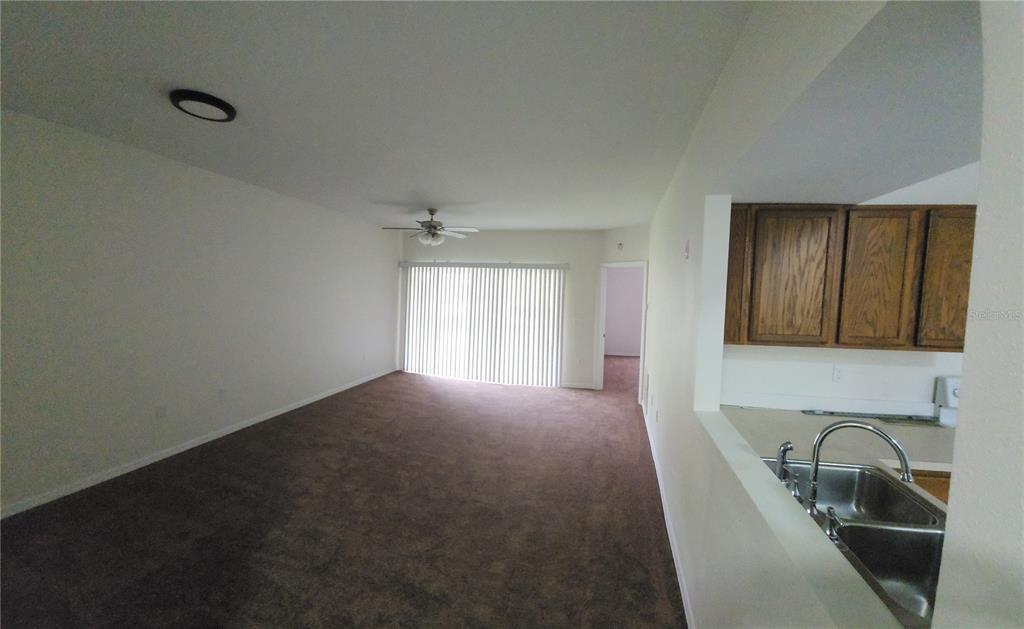 A living room with brown carpet and a ceiling fan overlooks a kitchen with cabinets — 9515 GROVEDALE CIRCLE UNIT 101, RIVERVIEW, FL