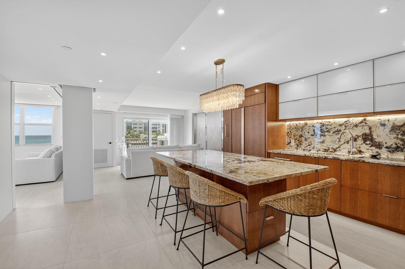 A modern kitchen features a granite island with wicker stools, wood cabinetry, and white uppers — 4511 S Ocean Boulevard # 507, Highland Beach FL 33487, HIGHLAND BEACH, FL