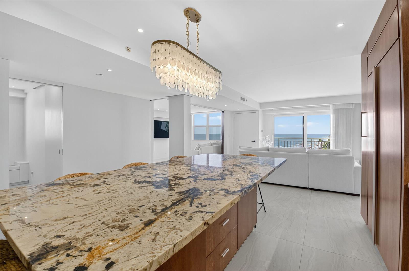 A kitchen island with a granite countertop sits in front of a living area overlooking ocean — 4511 S Ocean Boulevard # 507, Highland Beach FL 33487, HIGHLAND BEACH, FL