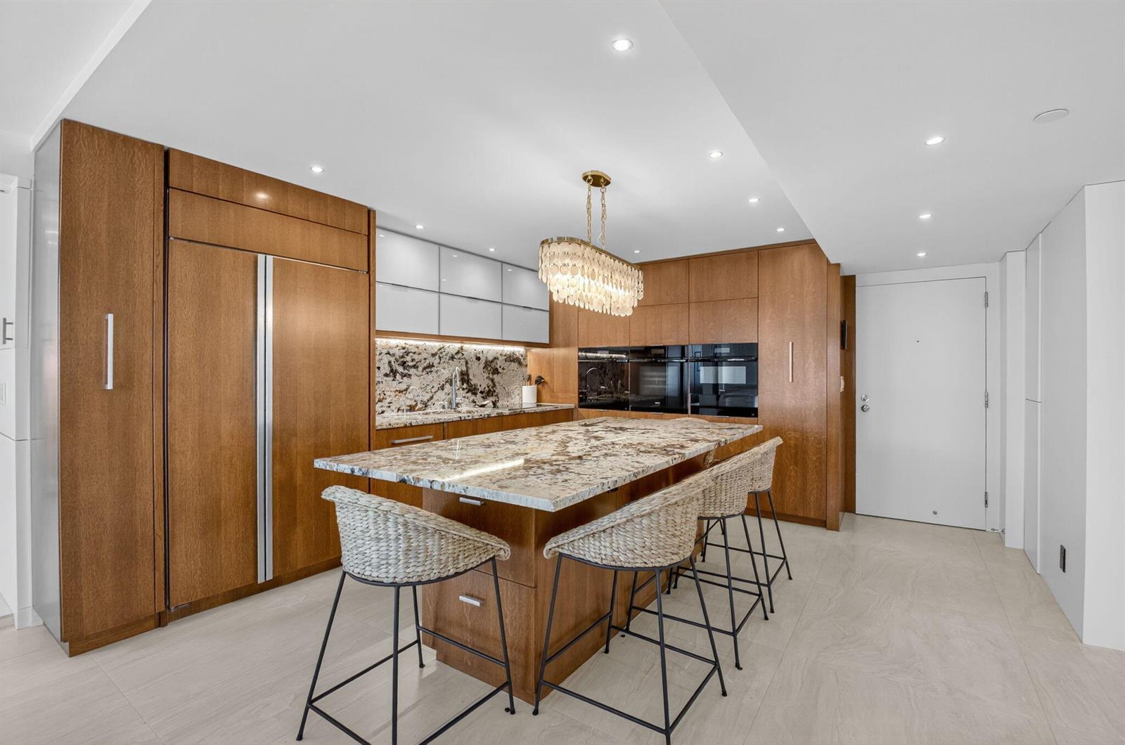 A modern kitchen features wood cabinetry, a large stone island, and three woven bar stools — 4511 S Ocean Boulevard # 507, Highland Beach FL 33487, HIGHLAND BEACH, FL