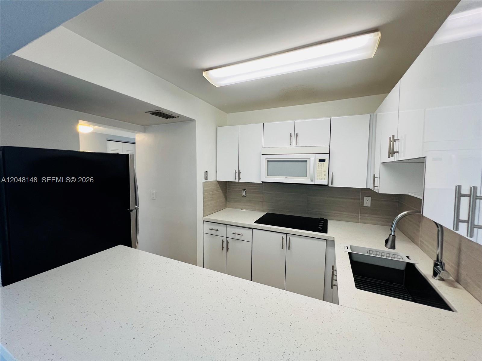 A kitchen features white cabinets, a black refrigerator, a black sink, and light-colored countertops — 8231 NW 8th St # 310, Miami FL 33126, MIAMI, FL