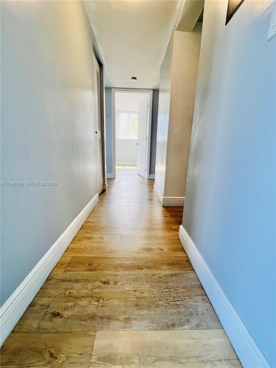 A hallway with light blue walls and wood-look flooring leads to an open doorway — 8231 NW 8th St # 310, Miami FL 33126, MIAMI, FL