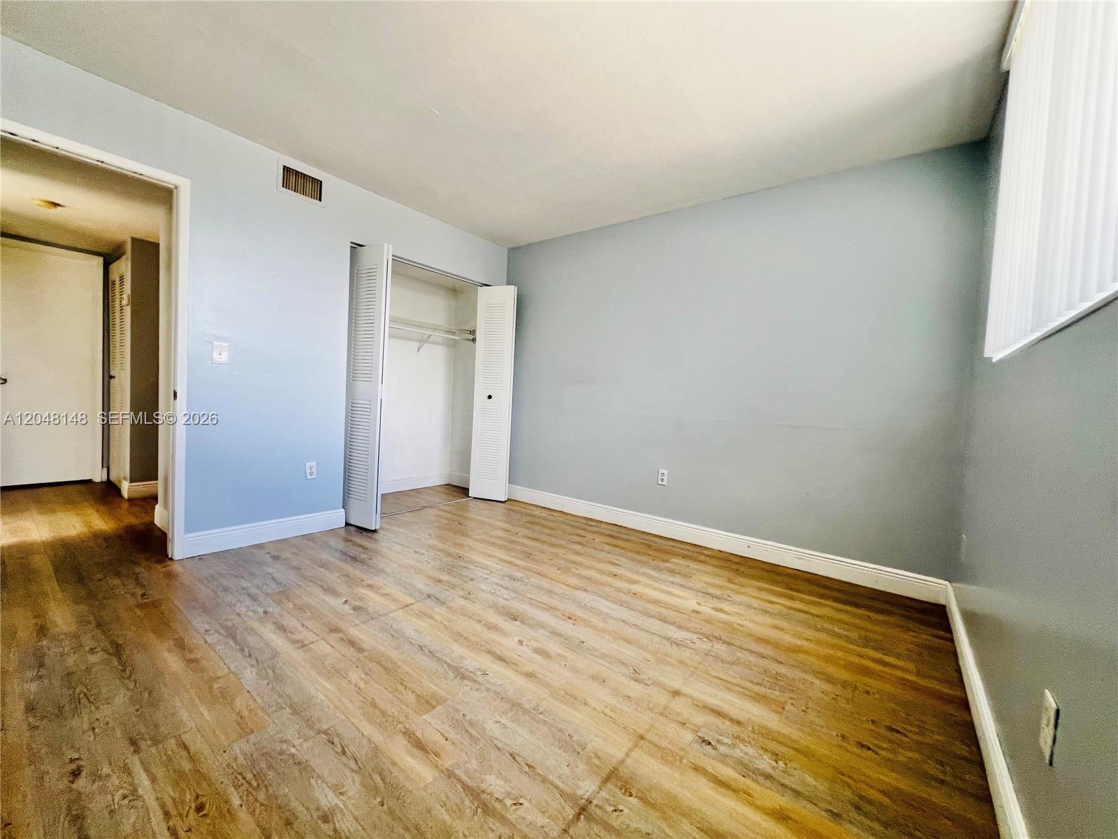 An empty bedroom features light blue walls, wood-look flooring, and an open closet — 8231 NW 8th St # 310, Miami FL 33126, MIAMI, FL