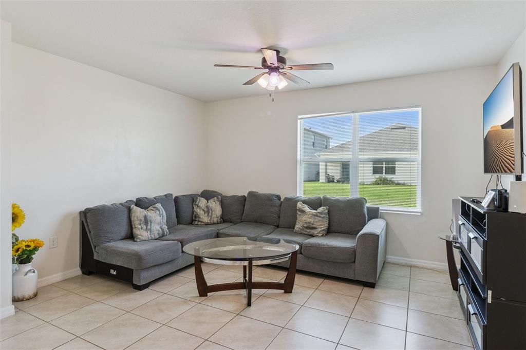 A living room features a gray sectional sofa, a glass coffee table, and tile flooring — 4013 SILVERSTREAM TERRACE, SANFORD, FL