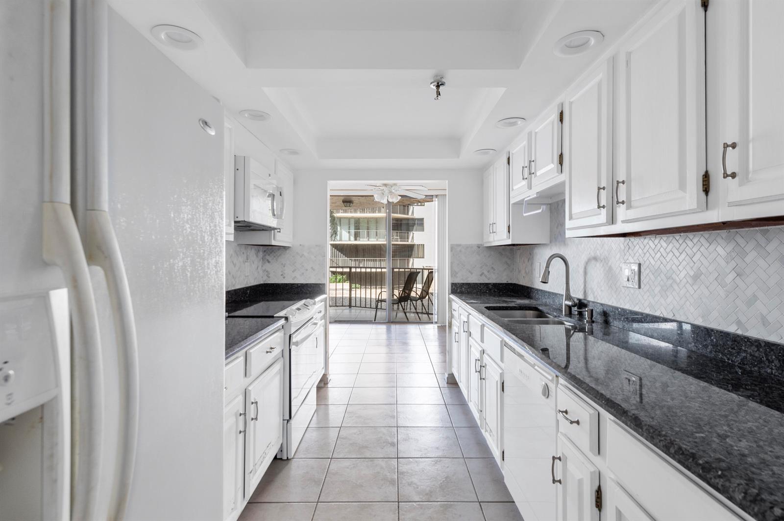 A galley kitchen features white cabinets, dark granite countertops, a herringbone backsplash, and tile flooring — 859 Jeffery Street # 312, Boca Raton FL 33487, BOCA RATON, FL