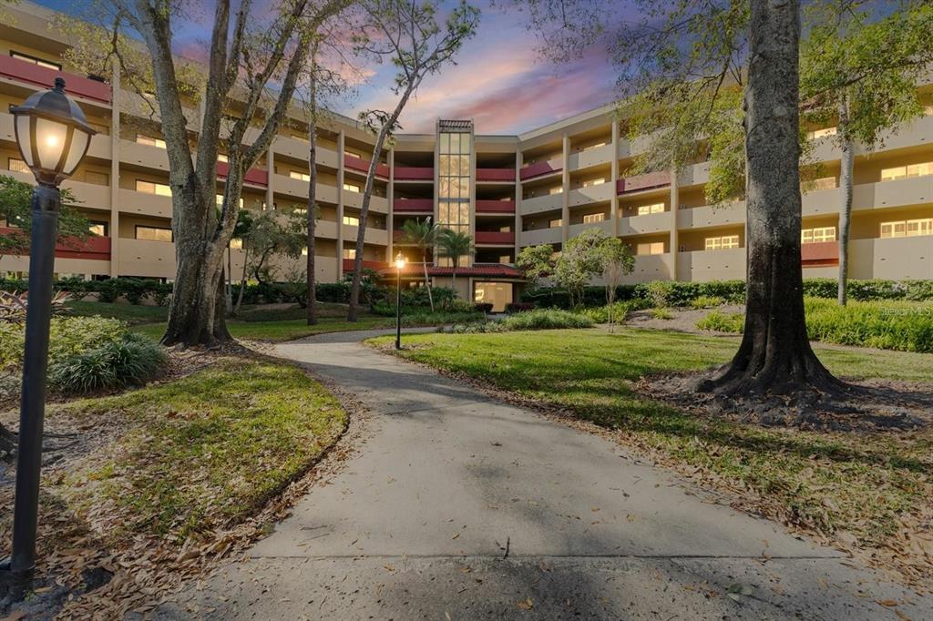 A paved walkway leads toward the entrance of a multi-story apartment building with exterior balconies — 3076 EASTLAND BOULEVARD UNIT 210, CLEARWATER, FL
