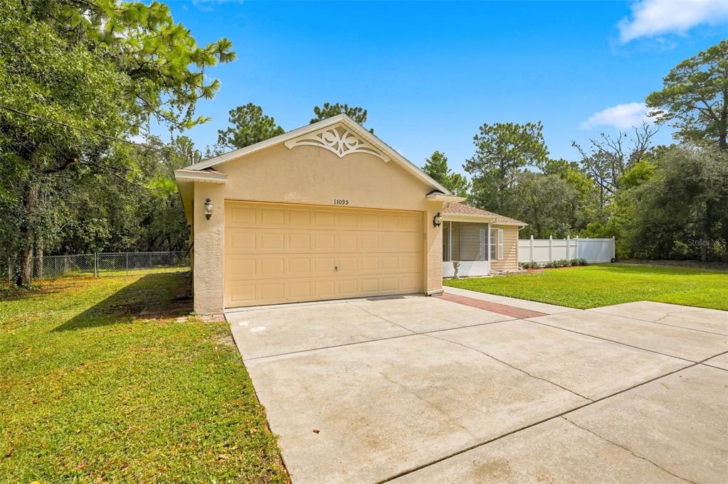 A beige house with a two-car garage and a concrete driveway sits on a lawn — 11095 FLATWOOD AVENUE, WEEKI WACHEE, FL