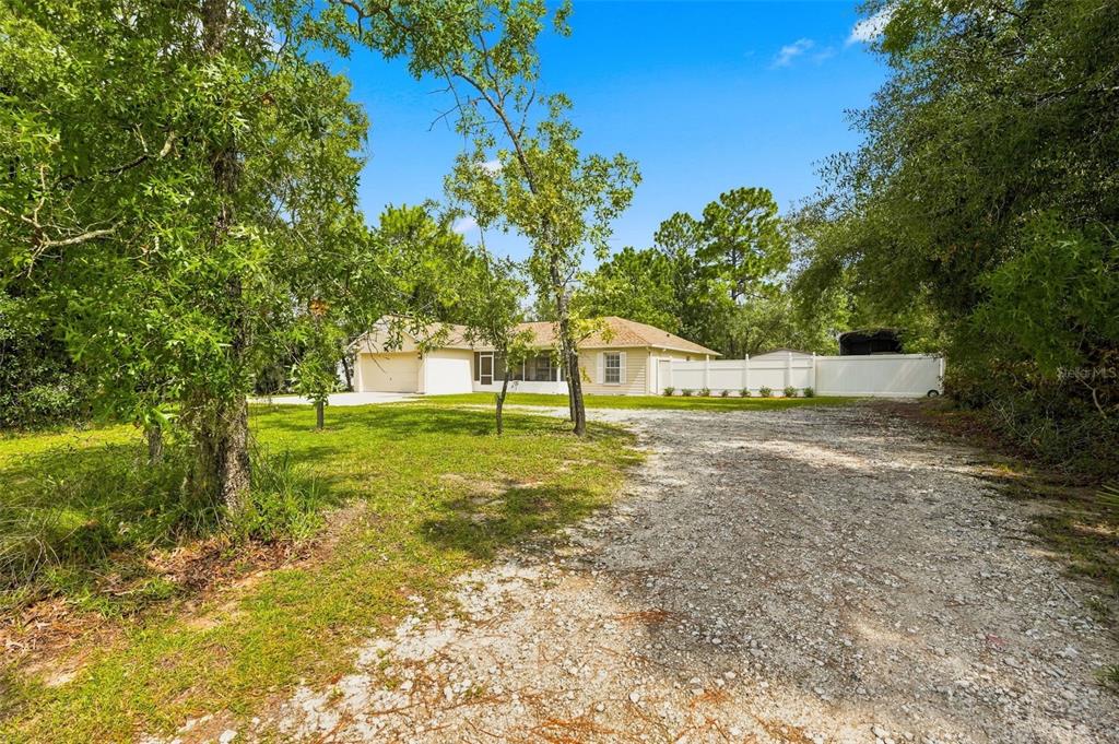 A single-story house with a gravel driveway and a white privacy fence sits among trees — 11095 FLATWOOD AVENUE, WEEKI WACHEE, FL