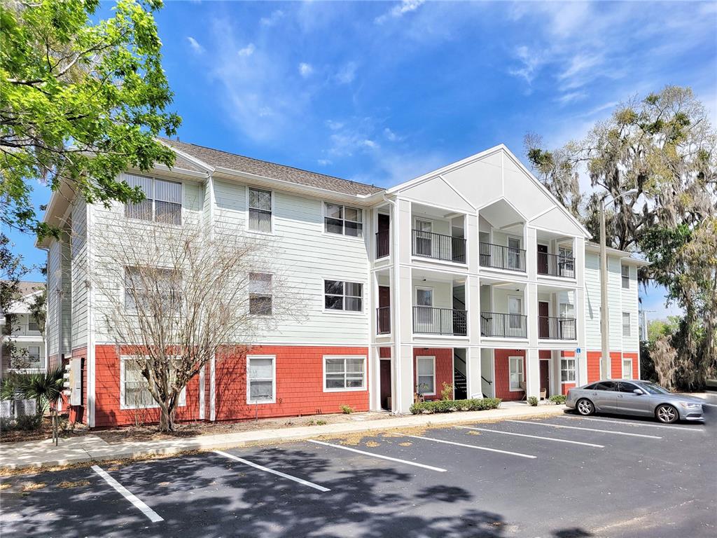 A three-story apartment building with light siding and red brick accents sits by a parking lot — 2360 SW ARCHER ROAD UNIT 505, GAINESVILLE, FL
