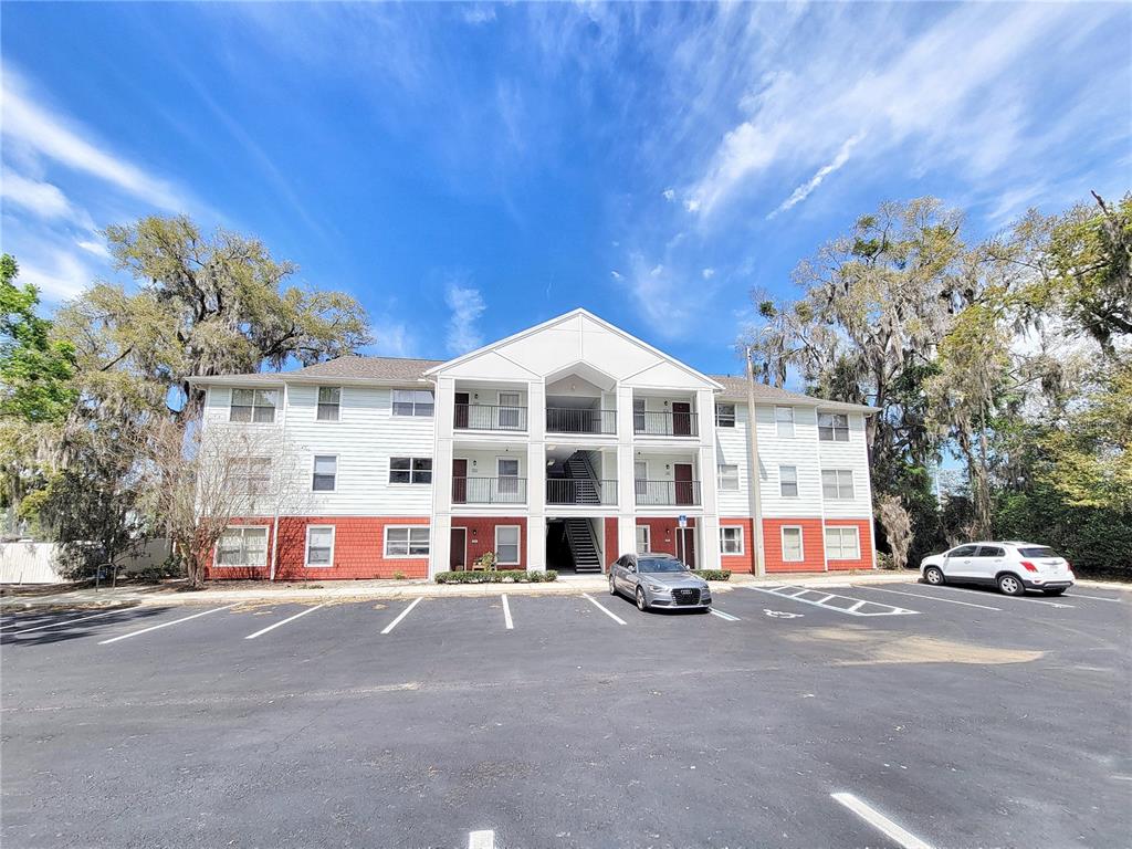 A three-story apartment building with white siding and red brick accents faces a parking lot — 2360 SW ARCHER ROAD UNIT 505, GAINESVILLE, FL