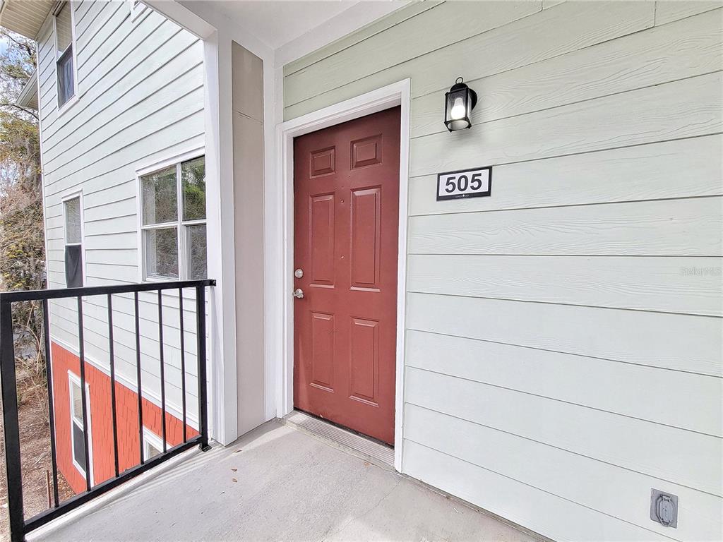 A red front door with the number 505 sits on a balcony with light-colored siding — 2360 SW ARCHER ROAD UNIT 505, GAINESVILLE, FL