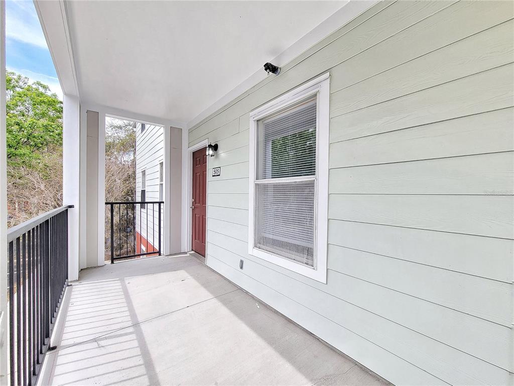 A covered balcony with light green siding, a red door, and a black metal railing — 2360 SW ARCHER ROAD UNIT 505, GAINESVILLE, FL