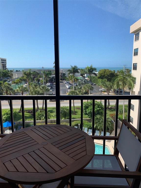 A balcony with a wooden table and chair overlooks a parking lot and the ocean — 1001 BENJAMIN FRANKLIN DRIVE UNIT 508, SARASOTA, FL