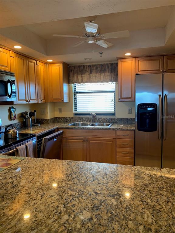 A kitchen features light wood cabinets, granite countertops, stainless steel appliances, and a ceiling fan — 1001 BENJAMIN FRANKLIN DRIVE UNIT 508, SARASOTA, FL