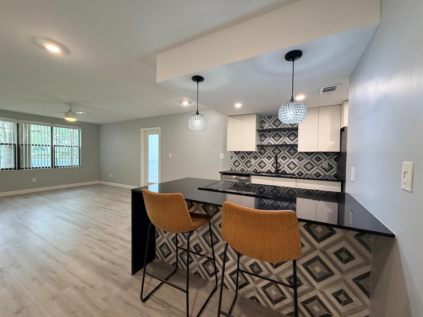 A kitchen with a black countertop island, patterned tile, and two bar stools faces a room — 4501 W Mcnab Road # 11, Pompano Beach FL 33069, POMPANO BEACH, FL