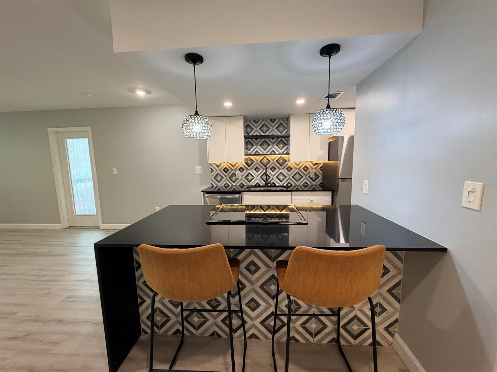 A kitchen features a black waterfall island with bar stools and geometric patterned tile backsplash — 4501 W Mcnab Road # 11, Pompano Beach FL 33069, POMPANO BEACH, FL