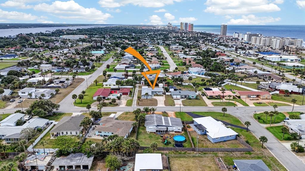 An aerial view shows a residential neighborhood with houses, streets, and a distant coastline — 1027 BEL AIRE DRIVE, DAYTONA BEACH, FL
