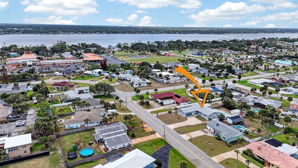 An aerial view shows a residential neighborhood with a house highlighted by an orange arrow — 1027 BEL AIRE DRIVE, DAYTONA BEACH, FL