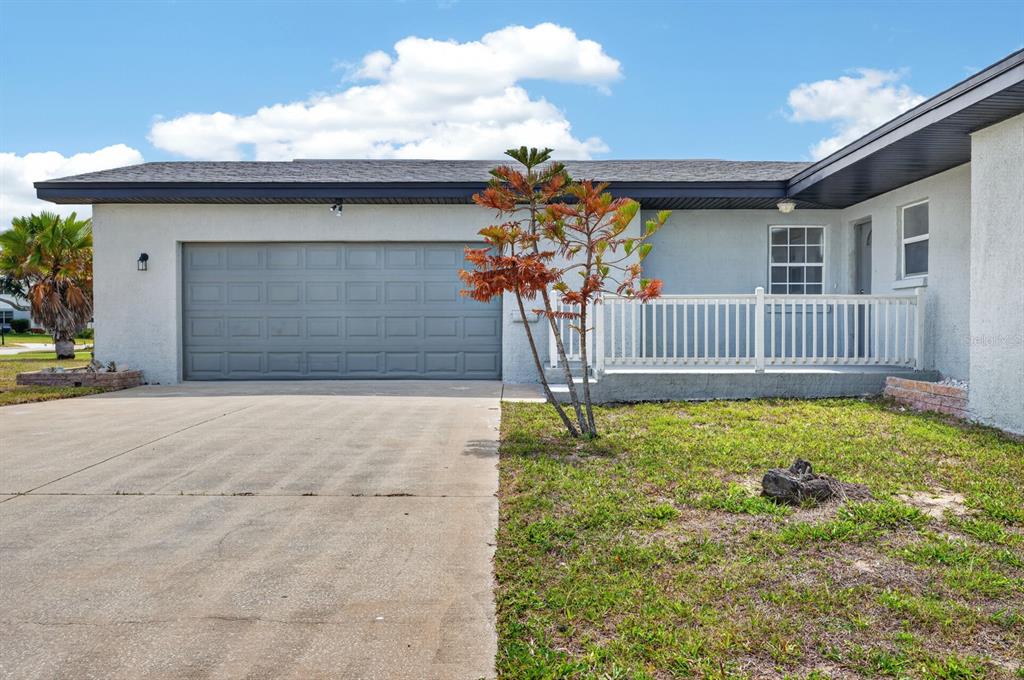 A single-story house exterior features a gray garage door, a concrete driveway, and a porch — 1027 BEL AIRE DRIVE, DAYTONA BEACH, FL