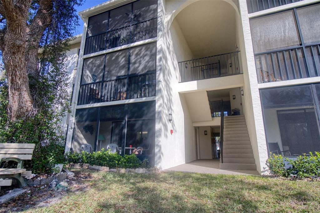 A three-story apartment building exterior features screened-in balconies, a concrete staircase, and a wooden bench — 3134 LAKE PINE WAY UNIT G2, TARPON SPRINGS, FL