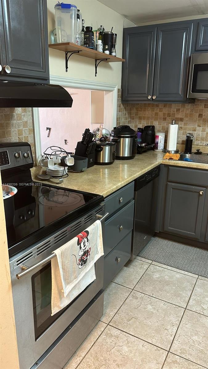 A kitchen features dark gray cabinets, a stainless steel stove, and a tan tile backsplash — 480 Executive Center Dr # 4L, West Palm Beach FL 33401, WEST PALM BEACH, FL