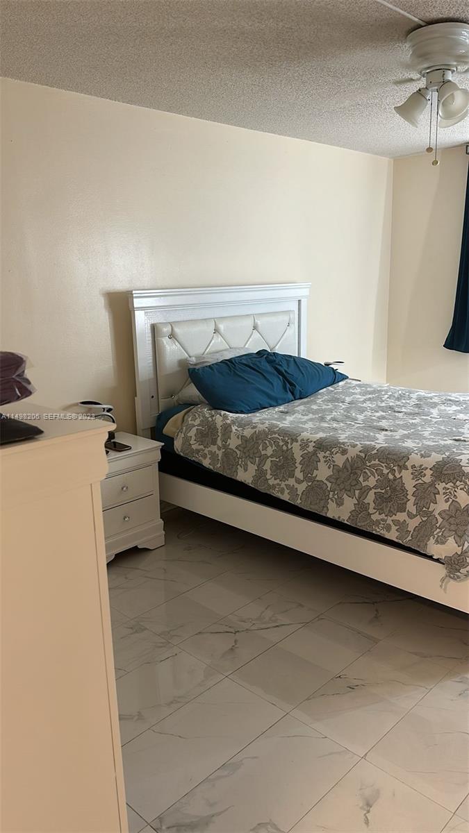 A bedroom features a white tufted headboard, a floral bedspread, and light-colored tile flooring — 480 Executive Center Dr # 4L, West Palm Beach FL 33401, WEST PALM BEACH, FL