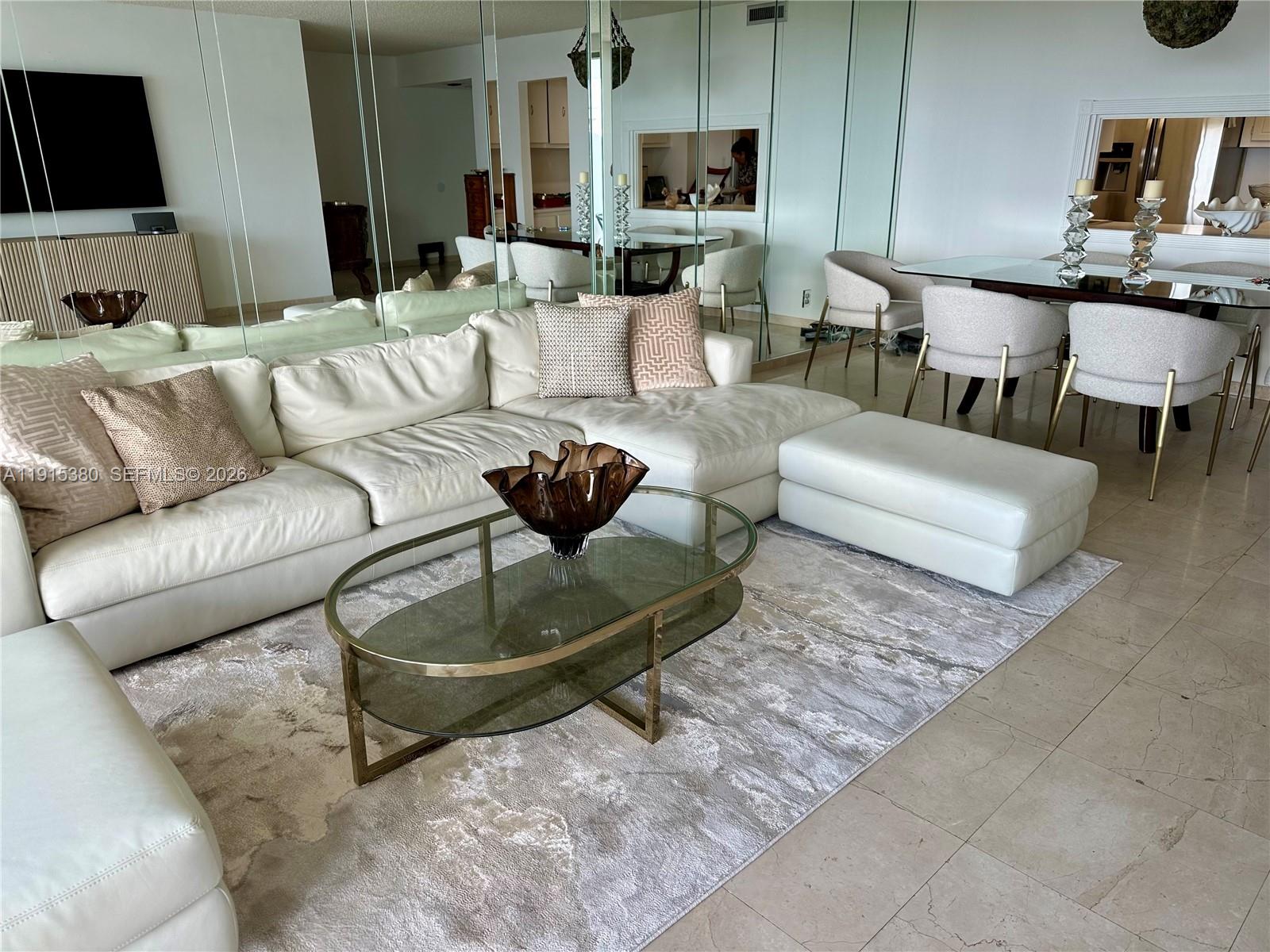 A living room features a white sectional sofa, glass coffee table, and mirrored walls — 199 Ocean Lane Dr # 1004, Key Biscayne FL 33149, KEY BISCAYNE, FL