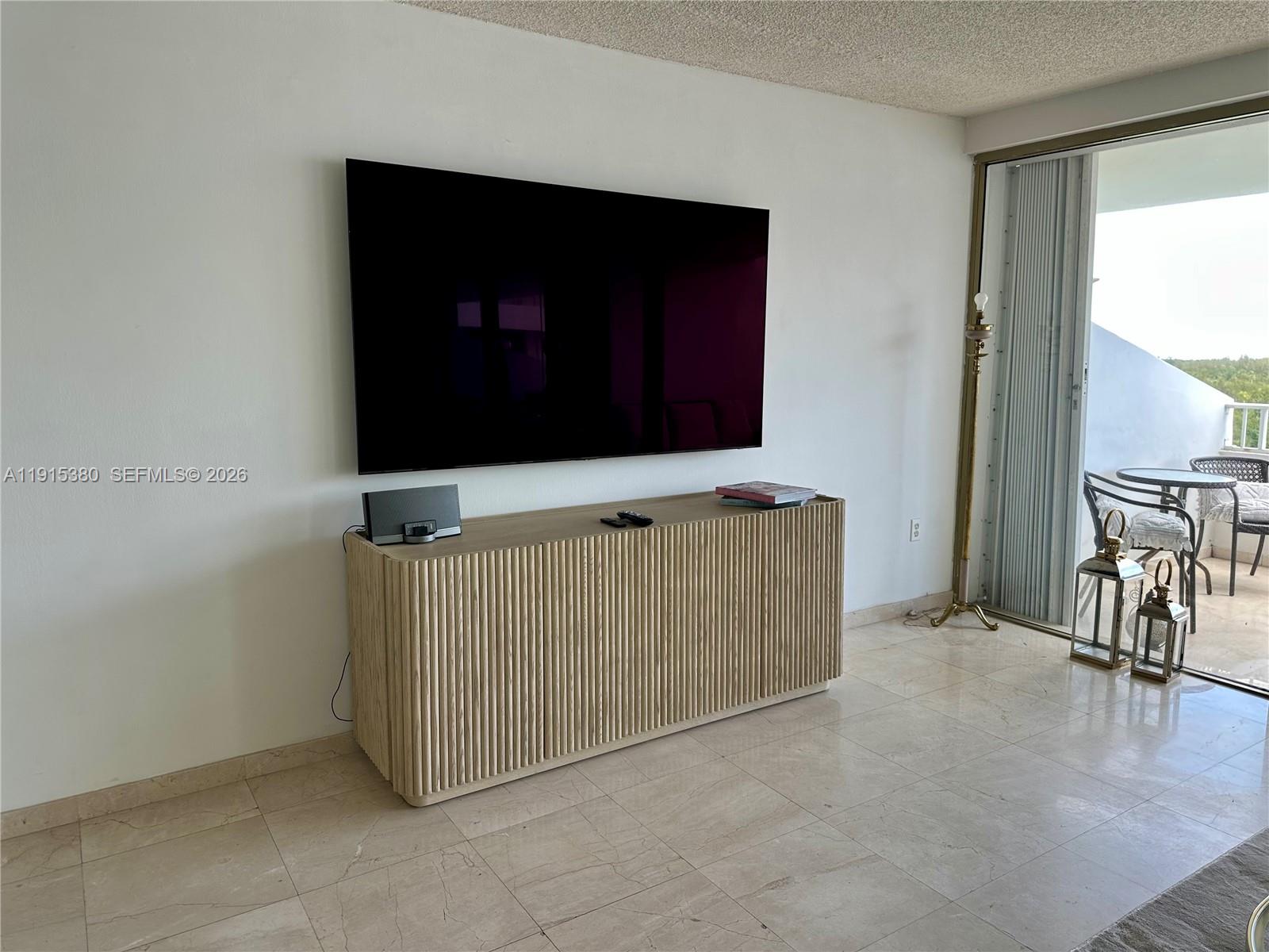 A living room features a wall-mounted television above a fluted wooden console on tile flooring — 199 Ocean Lane Dr # 1004, Key Biscayne FL 33149, KEY BISCAYNE, FL