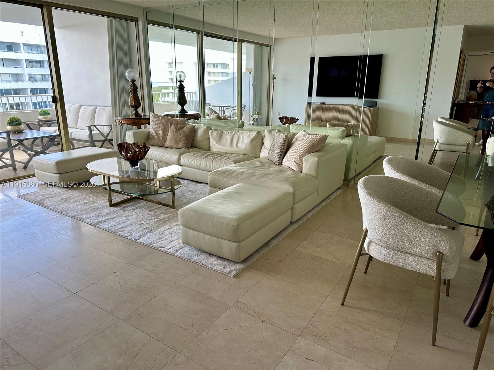 A living room features a large white sectional sofa, glass coffee table, and mirrored walls — 199 Ocean Lane Dr # 1004, Key Biscayne FL 33149, KEY BISCAYNE, FL