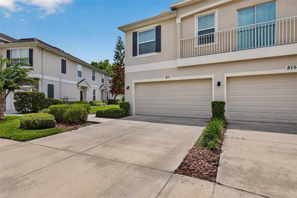 The exterior of a two-story townhouse features a beige facade, a two-car garage, and landscaping — 817 ASHENTREE DRIVE, PLANT CITY, FL