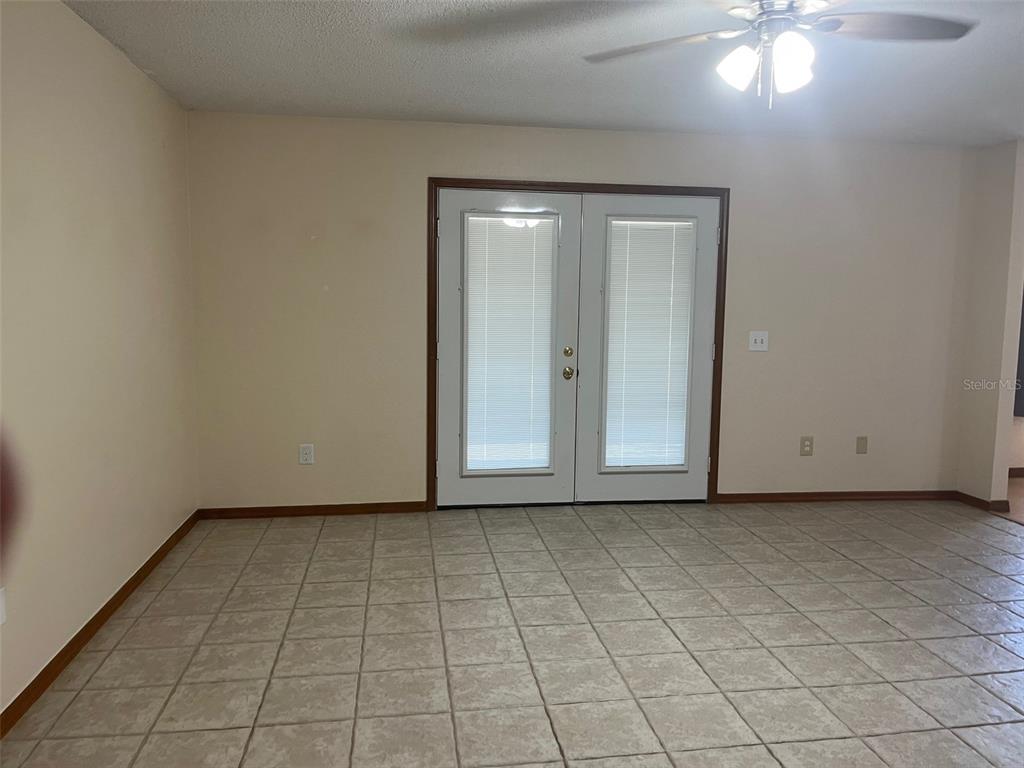 An empty room with beige tile flooring, light-colored walls, and a set of French doors — 175 CONRAD STREET, PORT ORANGE, FL