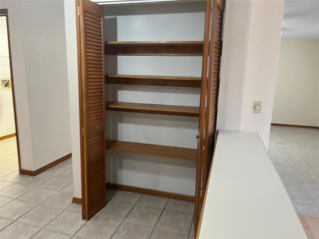 A pantry with wooden louvered doors and four interior shelves sits in a tiled room — 175 CONRAD STREET, PORT ORANGE, FL