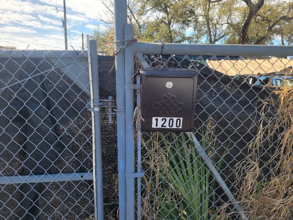 A black, locking mailbox with the number 1200 is mounted on a chain-link fence gate — 1200 29TH STREET, ORLANDO, FL