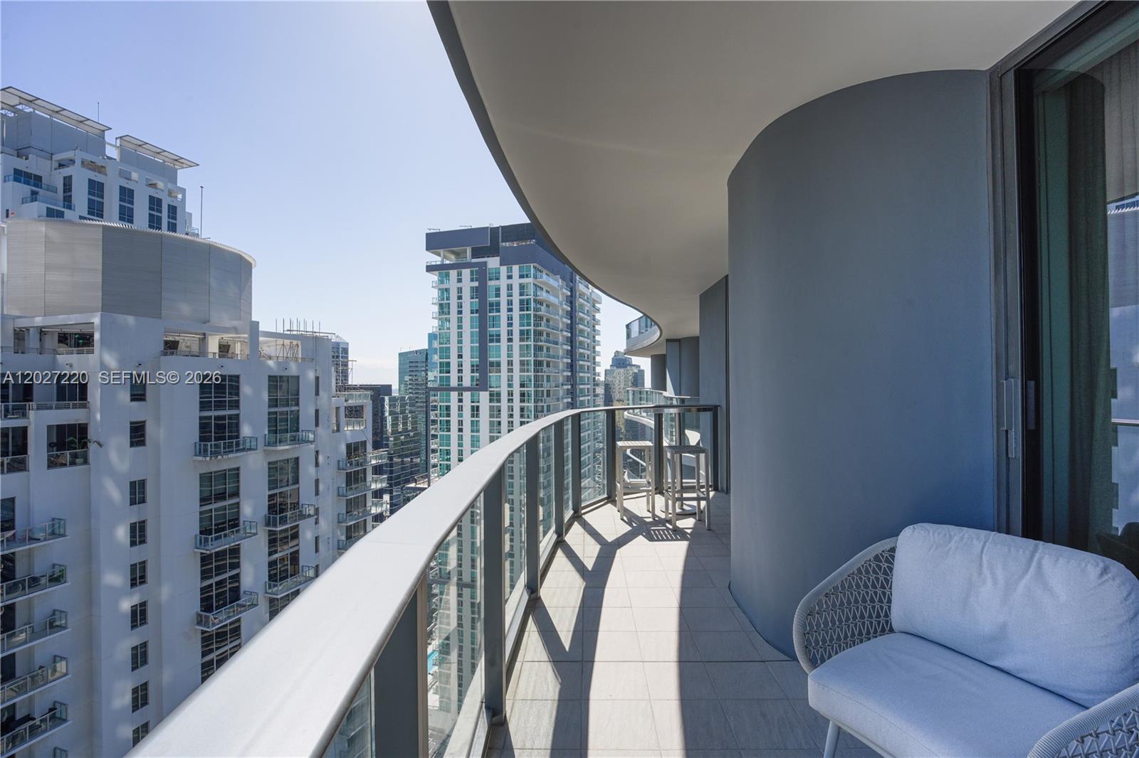 A curved balcony with light-colored tile flooring overlooks a dense city skyline — 1000 Brickell Plz # 3705, Miami FL 33131, MIAMI, FL