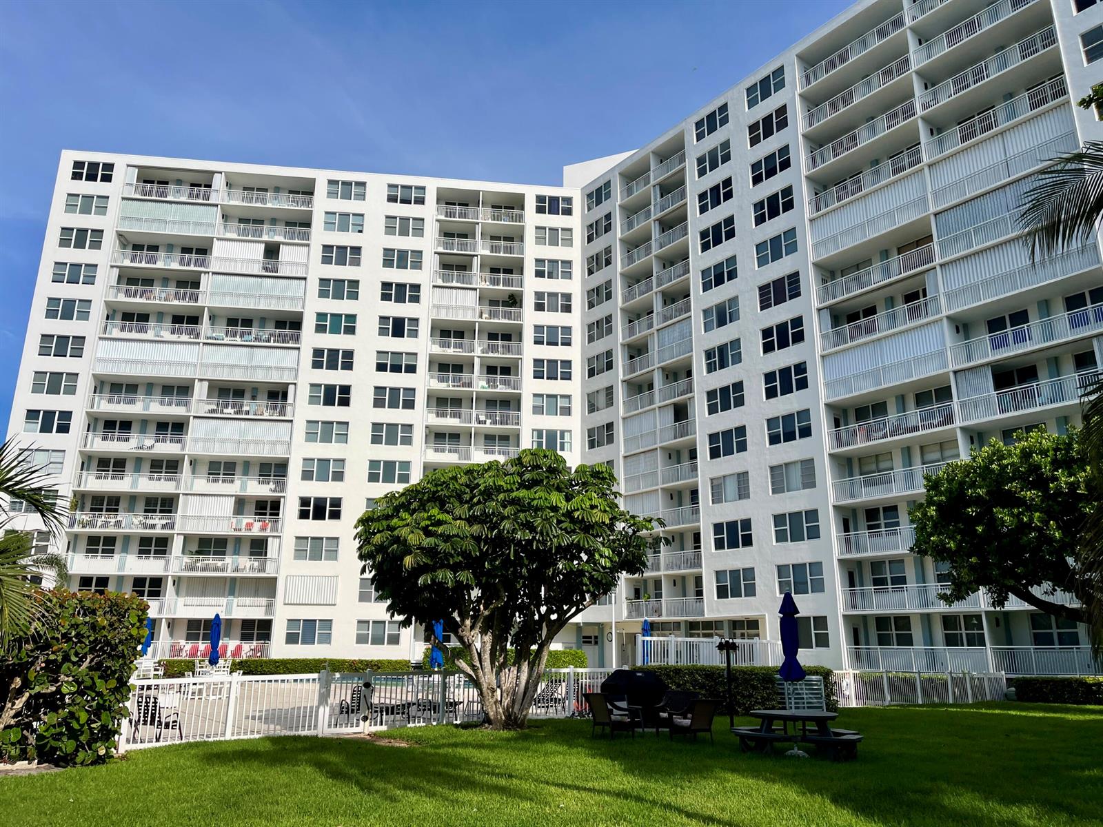 A large white multi-story apartment building with balconies overlooks a grassy lawn and pool area — 201 N Ocean Boulevard # 302, Pompano Beach FL 33062, POMPANO BEACH, FL