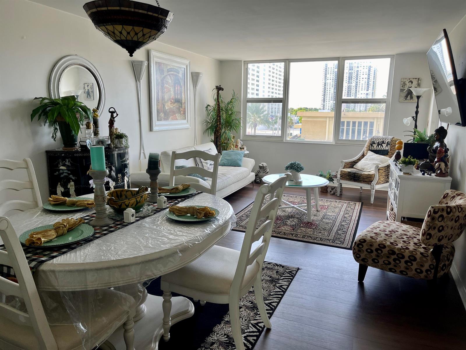 A bright living and dining area with white furniture, wood-look floors, and large windows — 201 N Ocean Boulevard # 302, Pompano Beach FL 33062, POMPANO BEACH, FL