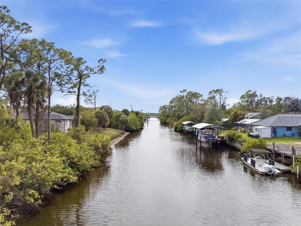 A canal flows between residential properties with boat docks and lush vegetation under a blue sky — 425 CHESHIRE STREET, PORT CHARLOTTE, FL