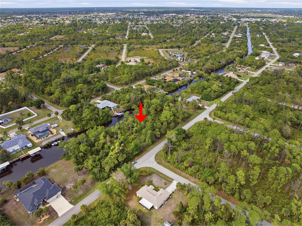 An aerial view shows a wooded, undeveloped waterfront lot marked by a red arrow — 425 CHESHIRE STREET, PORT CHARLOTTE, FL