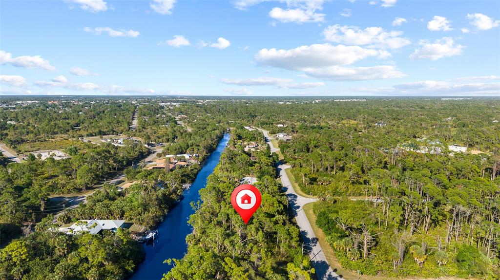 An aerial view shows a wooded lot adjacent to a canal with a location pin — 425 CHESHIRE STREET, PORT CHARLOTTE, FL
