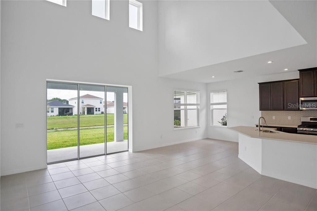 A bright, open-concept living area features high ceilings, tile flooring, and a kitchen with dark cabinets — 5719 MAIDENSTONE WAY, PALMETTO, FL