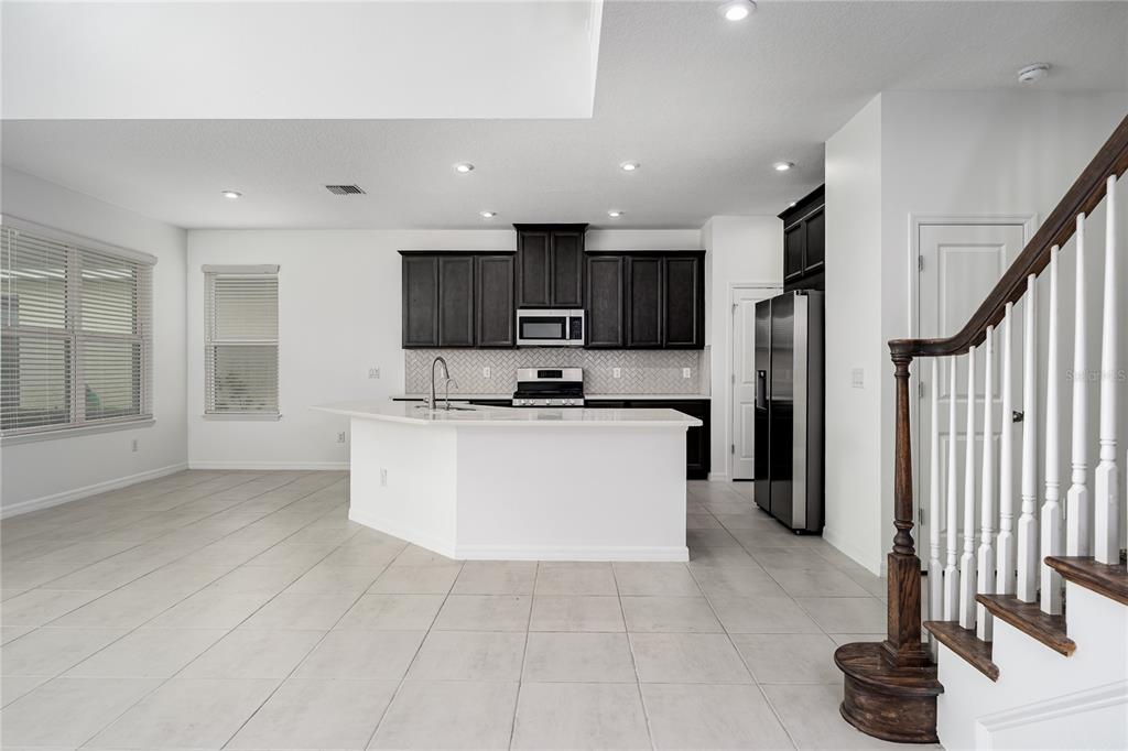 A kitchen with dark cabinets, white countertops, and tile flooring next to a wooden staircase — 5719 MAIDENSTONE WAY, PALMETTO, FL