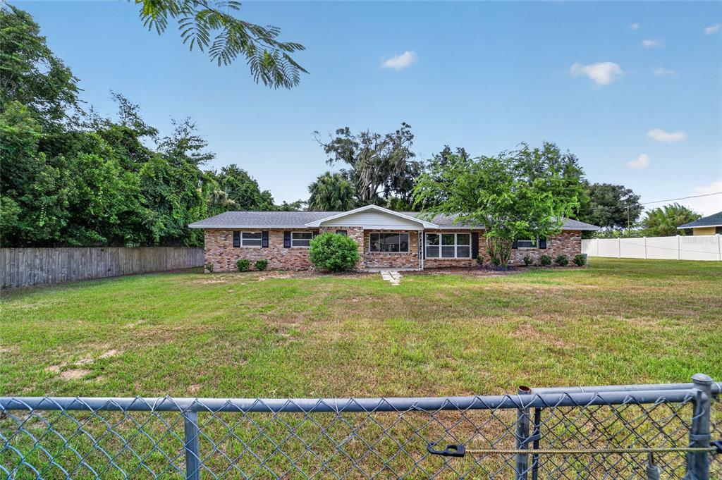 A single-story brick house with a gabled roof sits behind a chain-link fence — 2421 NE 57TH PLACE, OCALA, FL
