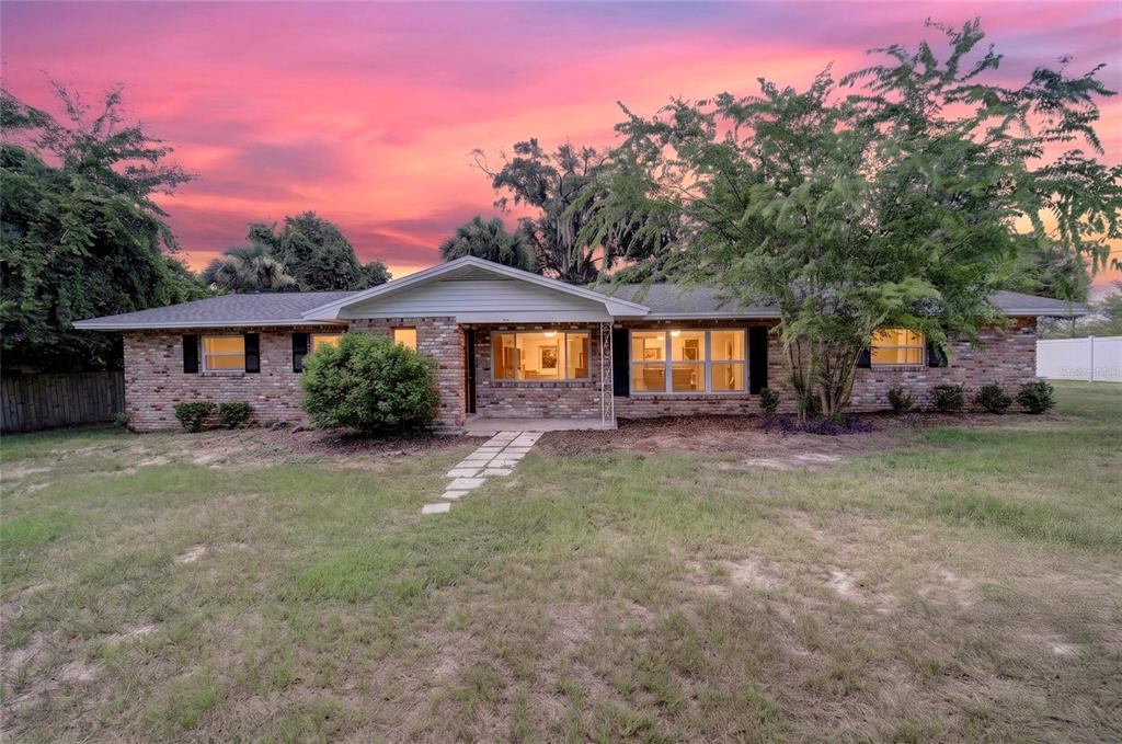 A single-story brick house with a front walkway stands under a vibrant sunset sky — 2421 NE 57TH PLACE, OCALA, FL