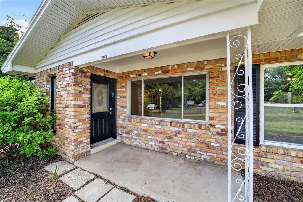 A brick house exterior features a covered concrete porch, a black front door, and decorative columns — 2421 NE 57TH PLACE, OCALA, FL