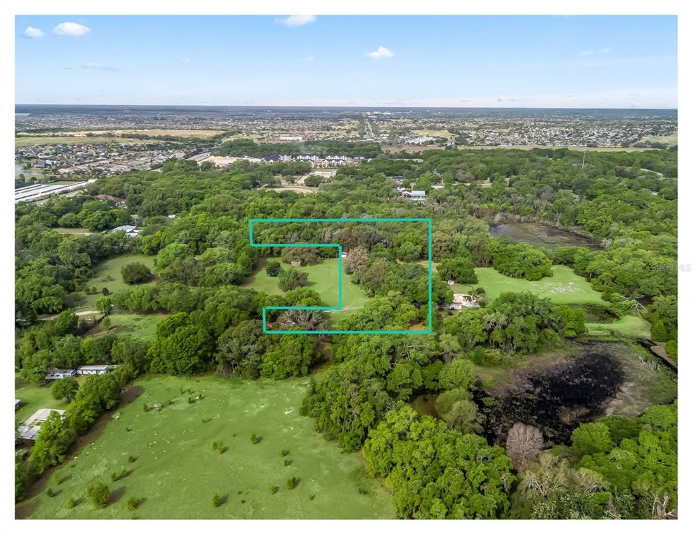 An aerial view shows a wooded plot of land outlined in blue within a landscape — 747 COUNTY ROAD 466A, FRUITLAND PARK, FL