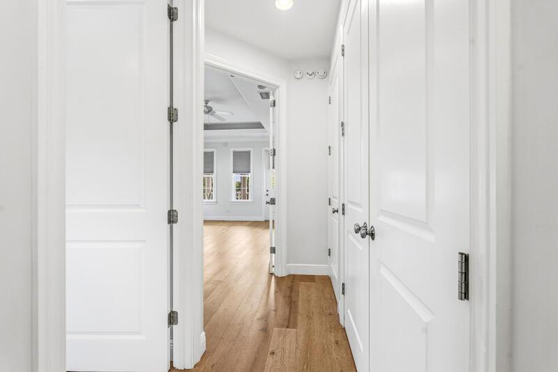 A hallway with white doors leads to a bright room with light wood flooring — VERO BEACH, FL