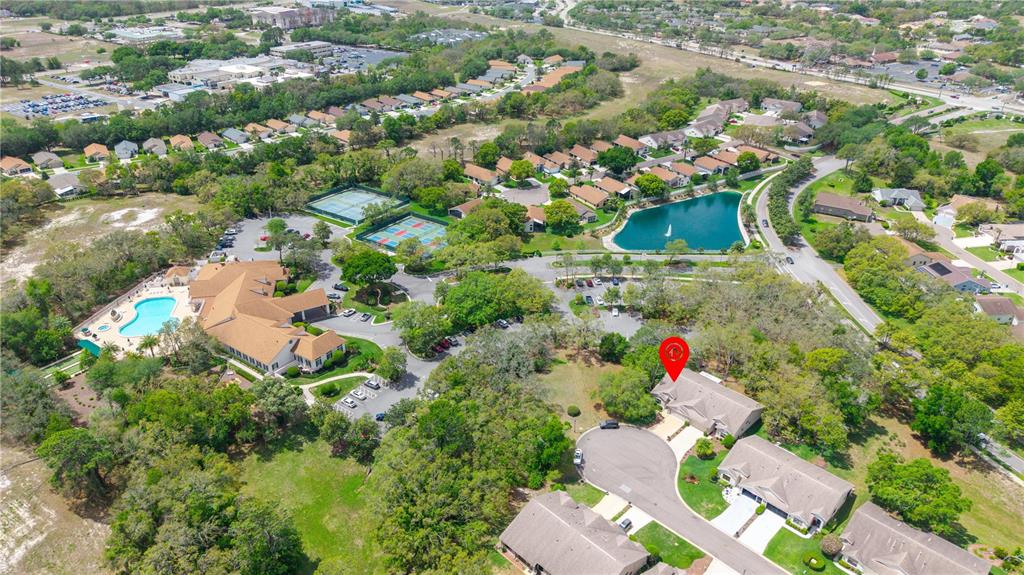 An aerial view shows a residential neighborhood with a community pool, tennis courts, and pond — 409 CANDLESTONE COURT, SPRING HILL, FL