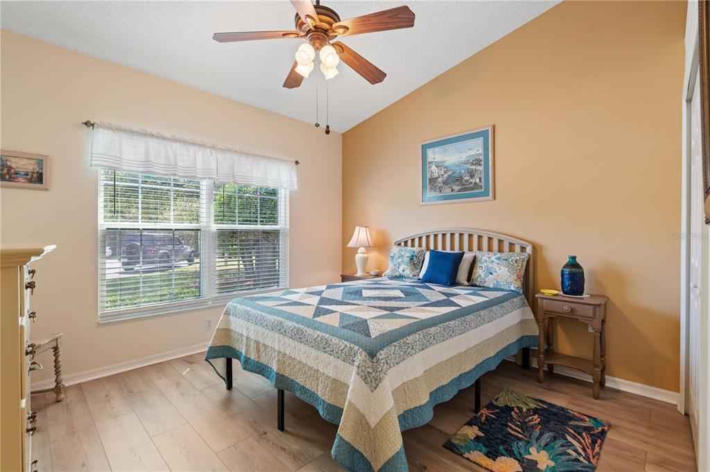 A bedroom features a quilt-covered bed, a ceiling fan, and light wood-look flooring — 409 CANDLESTONE COURT, SPRING HILL, FL
